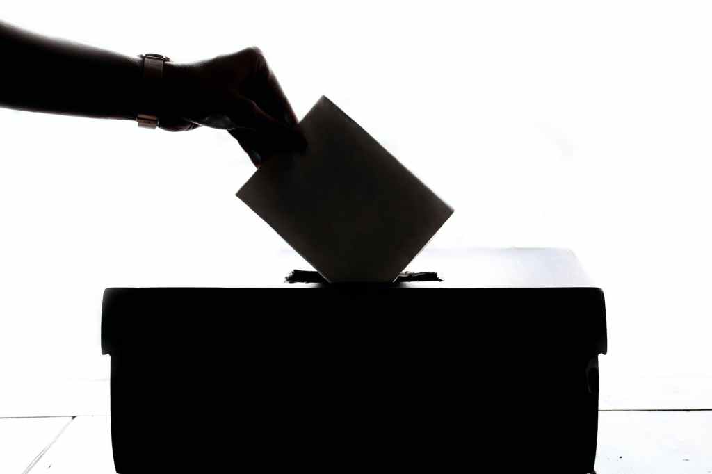 A shadowed hand putting a ballot into a ballot box.