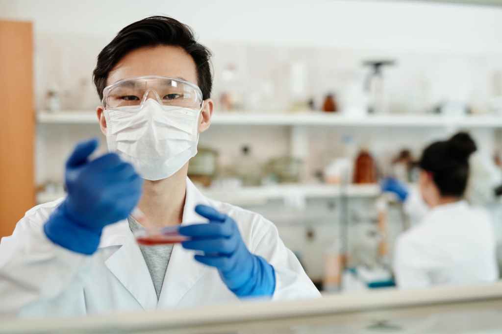 A man, with protective eyewear and face mask, in a lab to test a medicine.