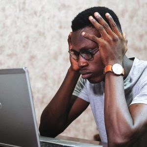 An image of a man sitting in front of his computer, looking stressed out.