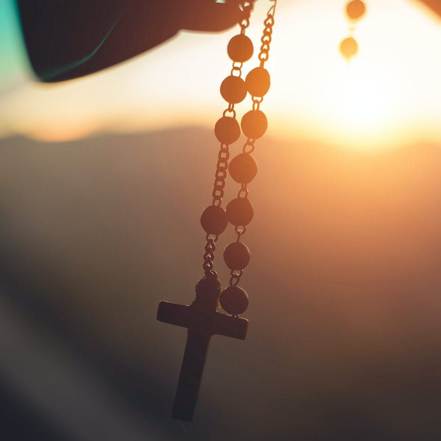 An image of someone holding a rosary, with a sunset in the background.