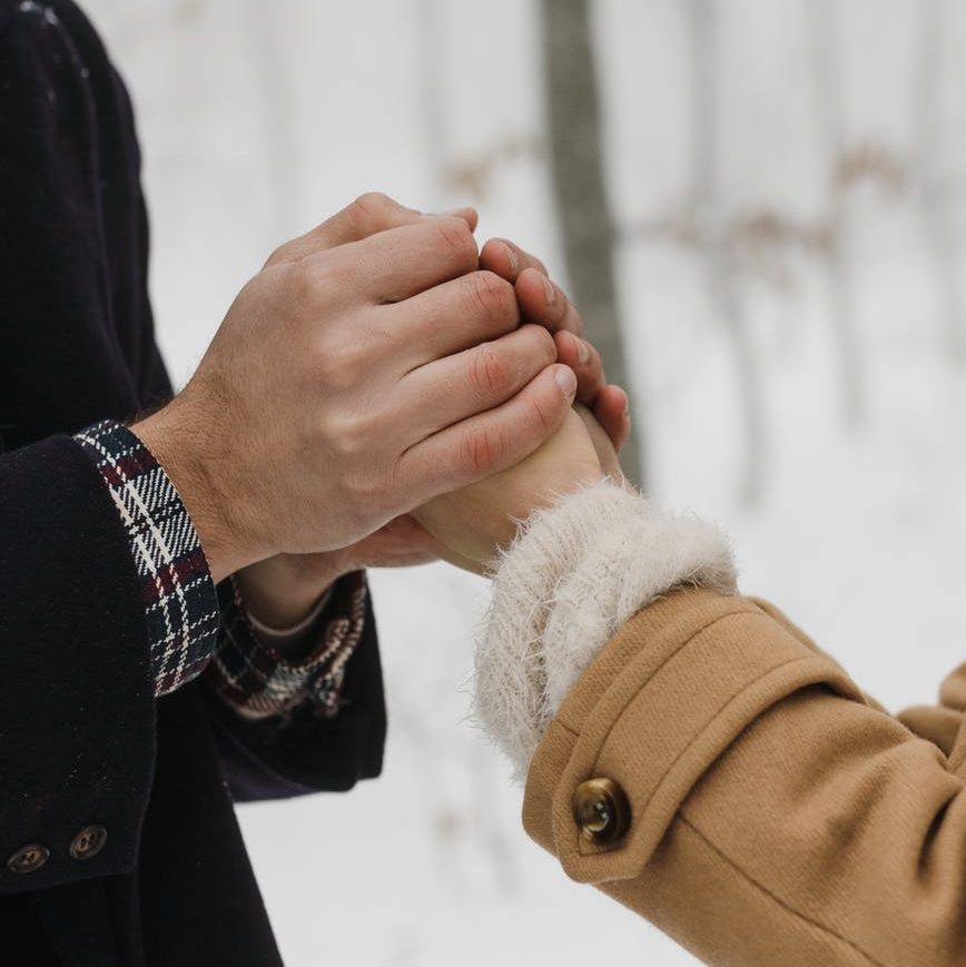 A couple's hands being clasped together. There is snow in the background.
